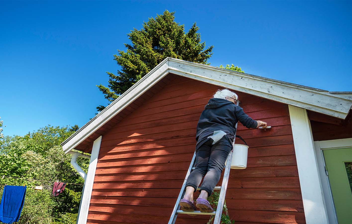 Schützen auch Sie Ihre Holzfassade für Witterungseinflüssen Eine Frau streicht eine Holzfassade im typischen Schwedenrot